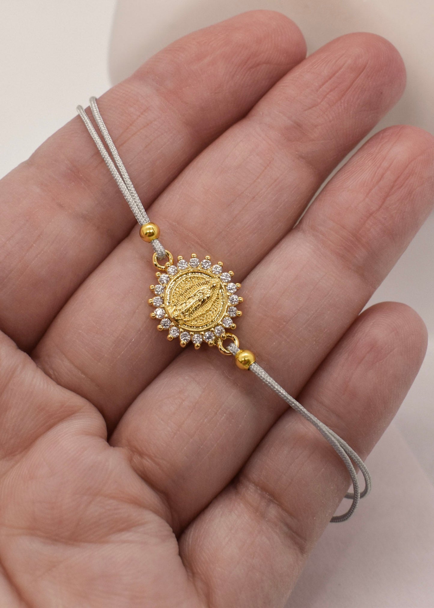 Gold bracelet with a decorative charm held in a hand against a neutral background