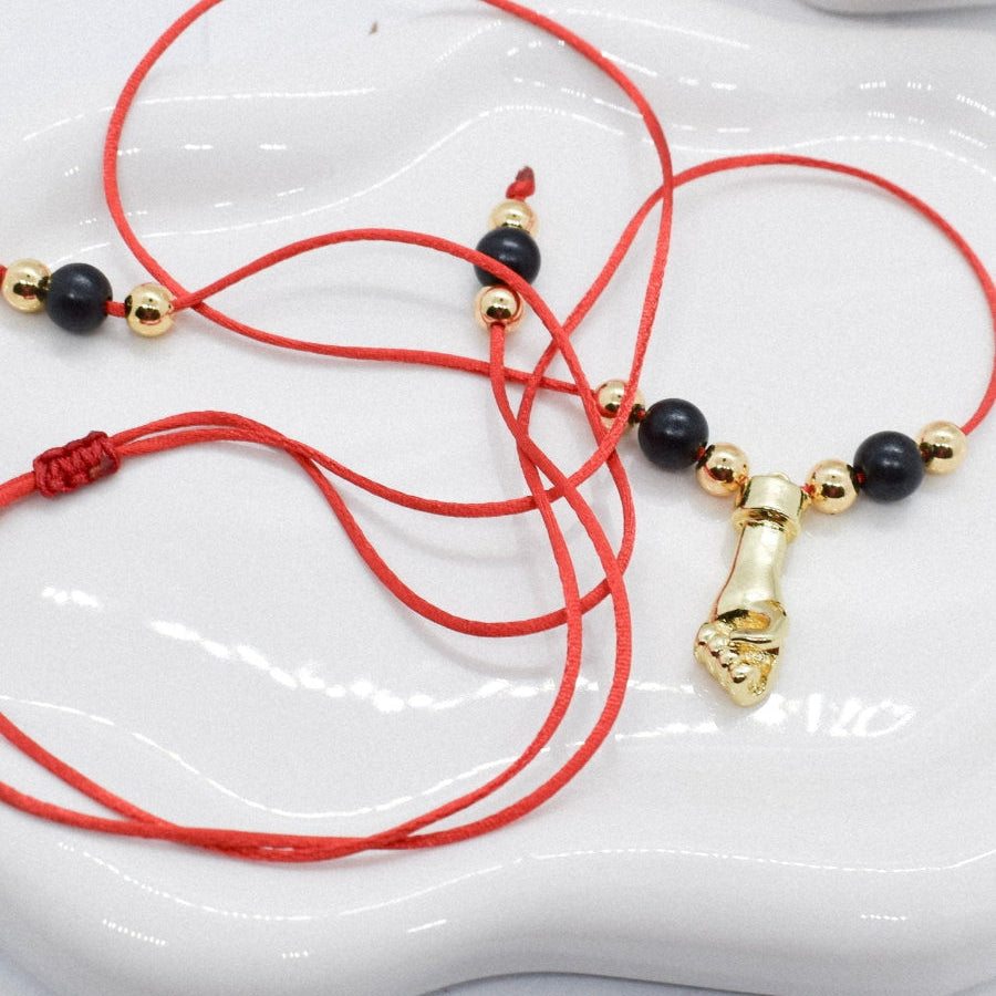 Red cord bracelet with black and gold beads and a hand charm on a white dish