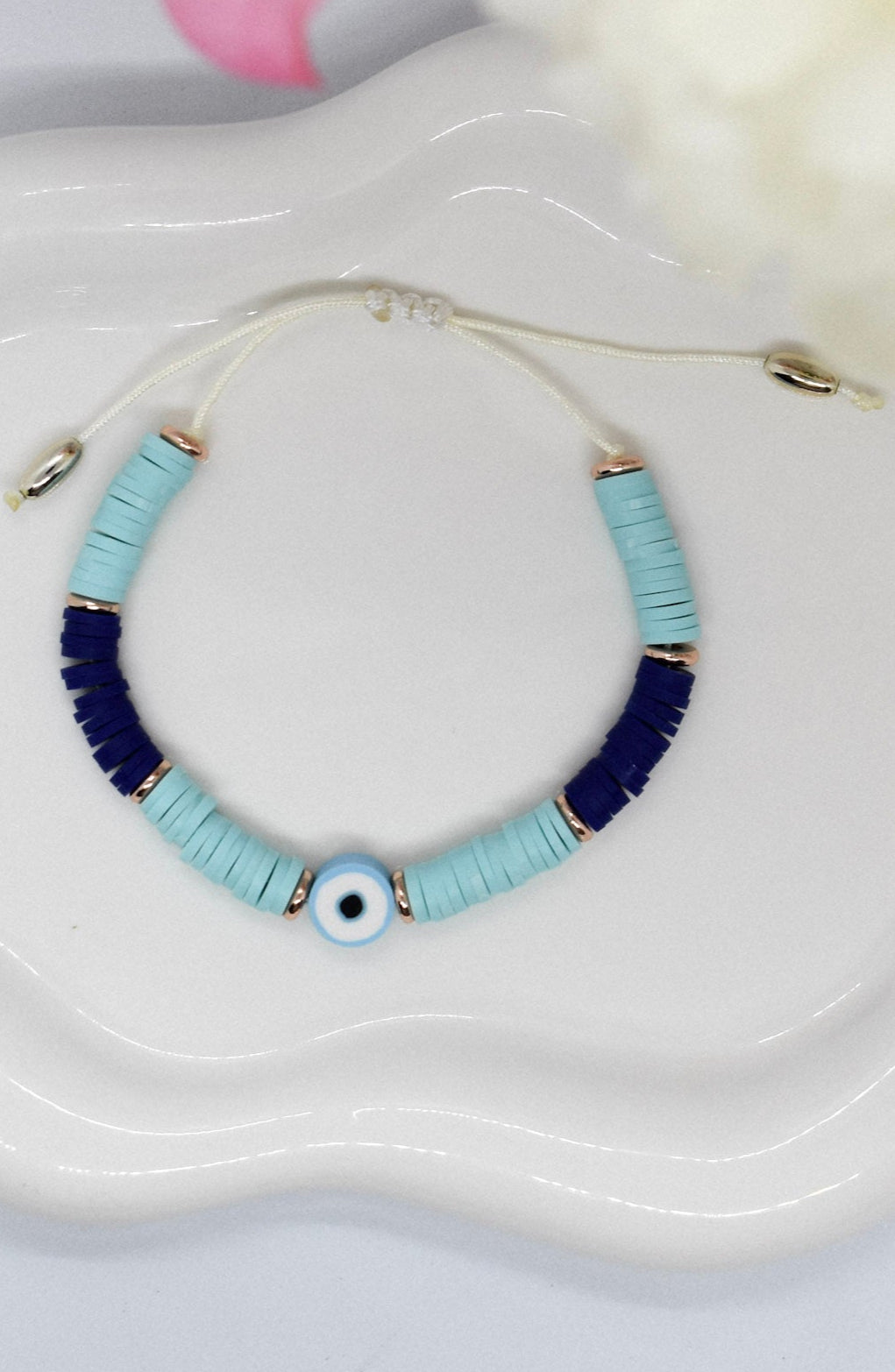 Bracelet with blue and gold beads on a white dish with flowers in the background