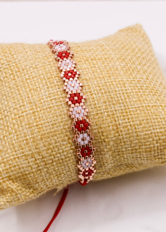 Beaded bracelet with red and white pattern on a textured beige surface