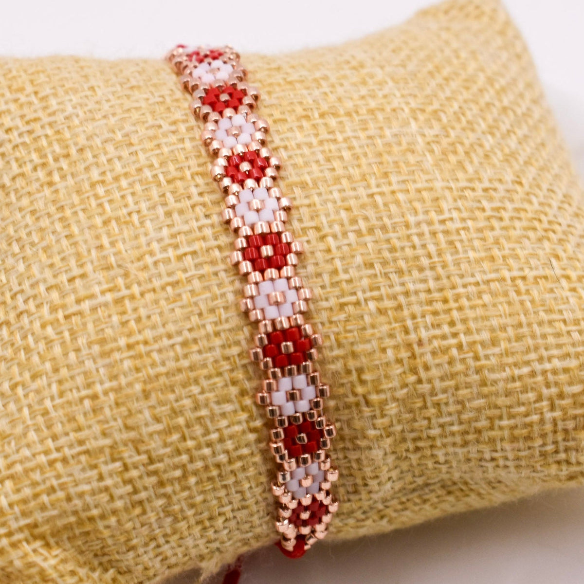 Beaded bracelet with red and white pattern on a textured beige surface