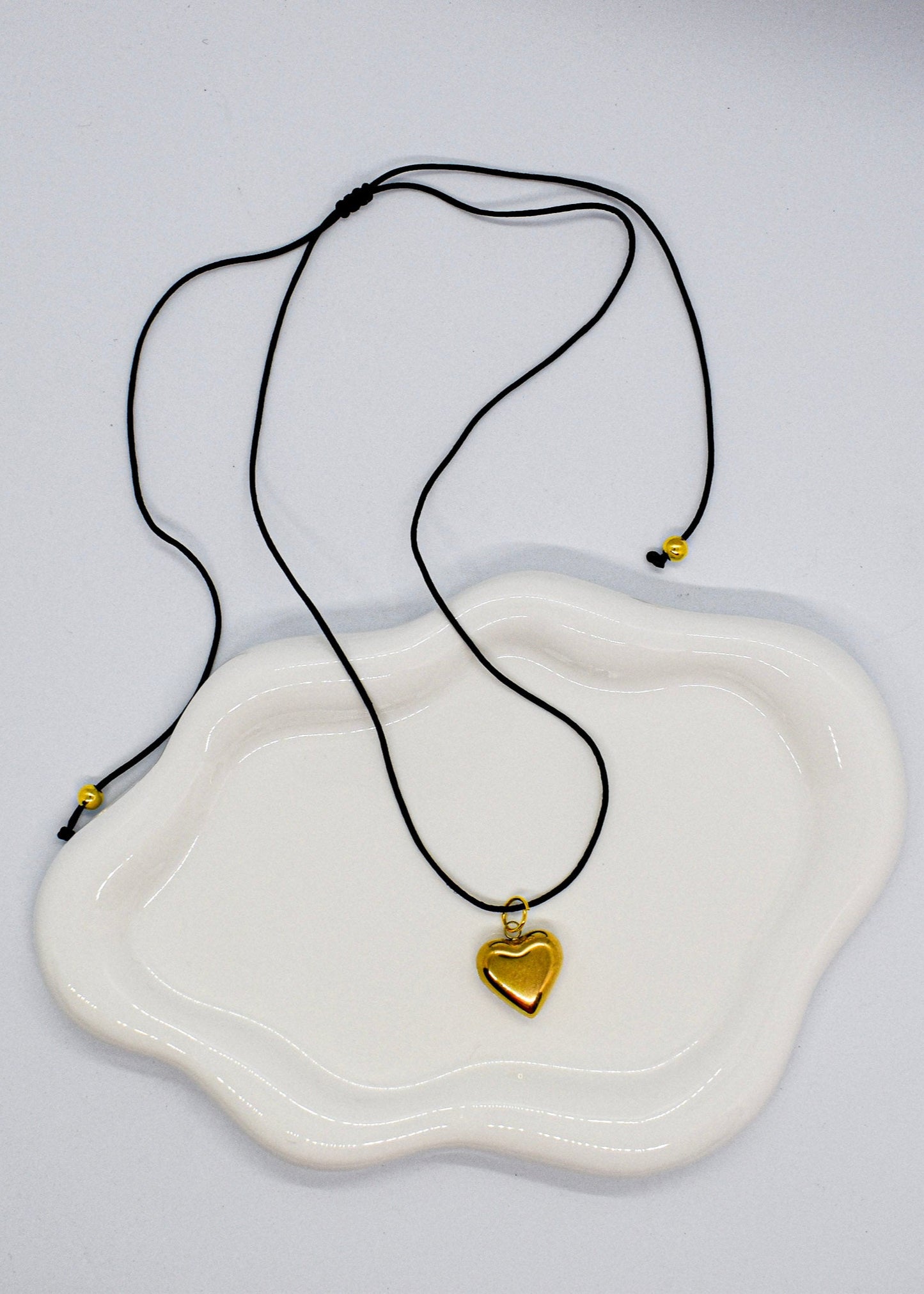 Necklace with a gold heart pendant on a white dish against a light gray background