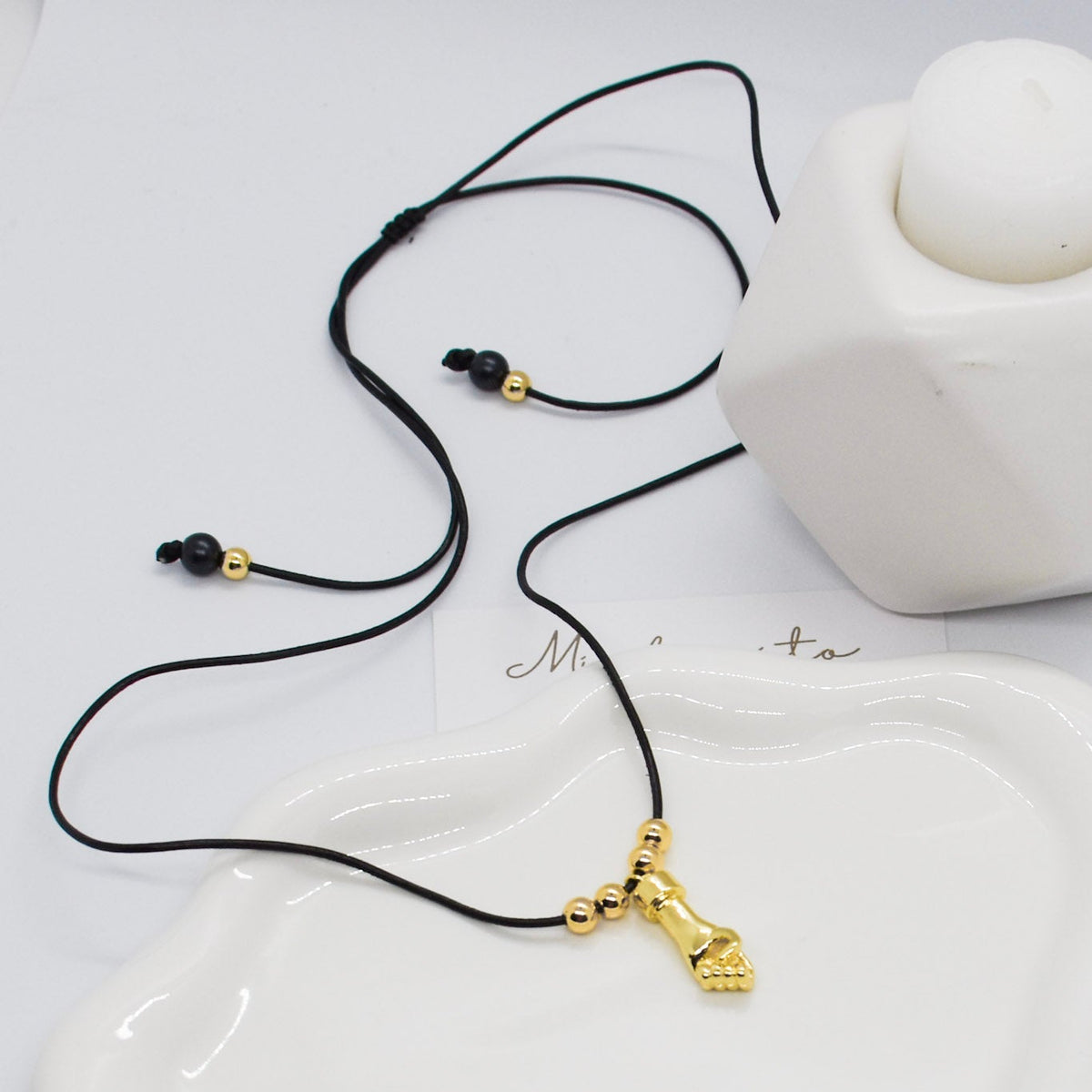 Necklace with a gold pendant on a white ceramic dish, with 'Minta' branding.