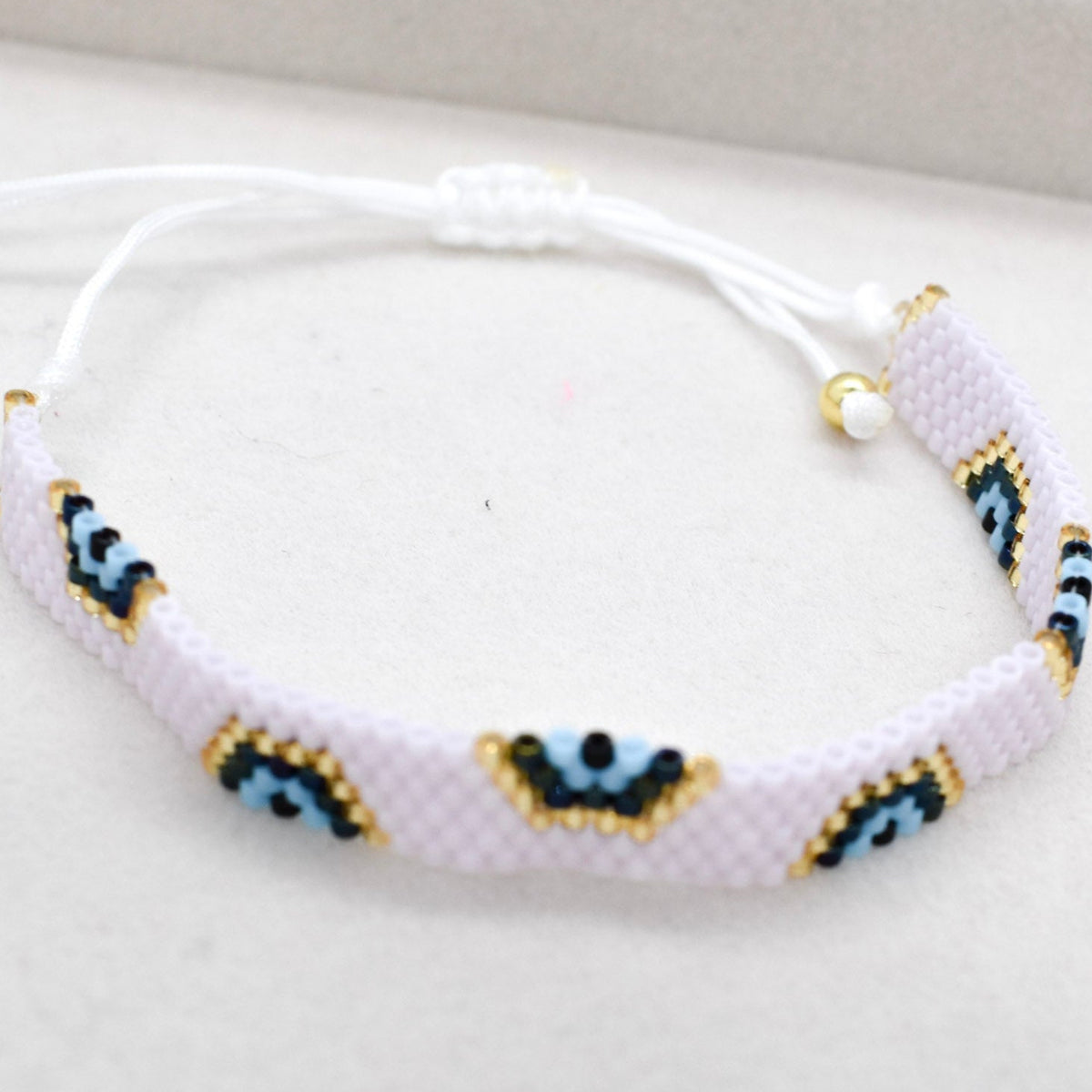 Pink bracelet with blue and gold evil eye pattern on a white background