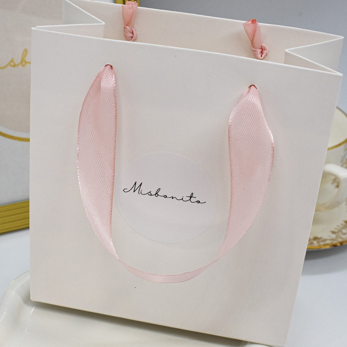 White gift bag with pink handles on a white surface