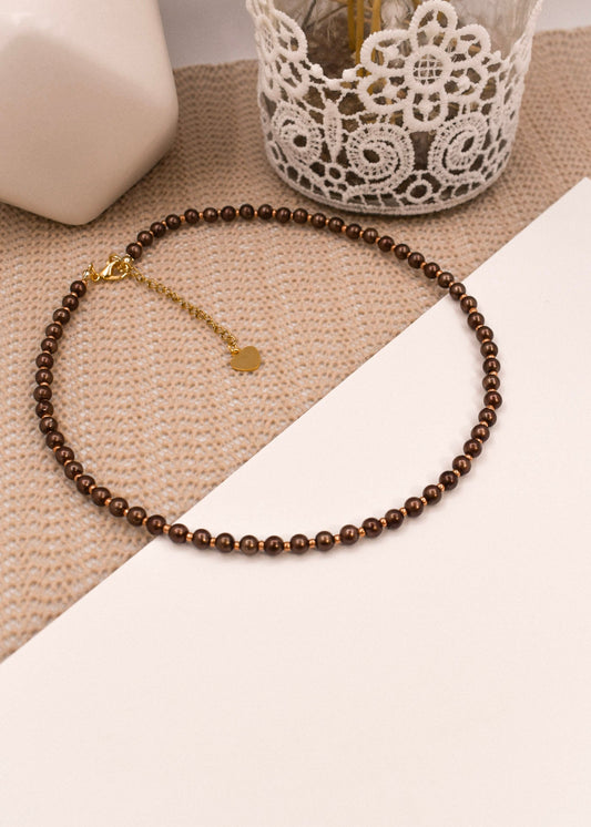 Brown beaded necklace with a gold clasp on a textured surface