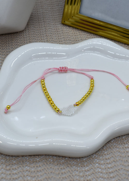 pink bracelet wit with gold beads, on a white ceramic dish.