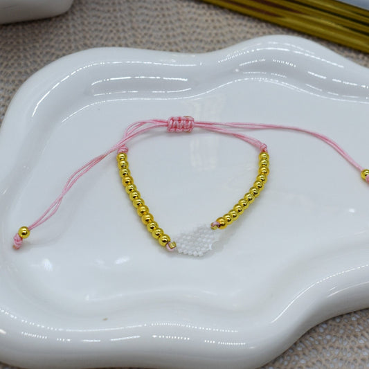 pink bracelet wit with gold beads, on a white ceramic dish.