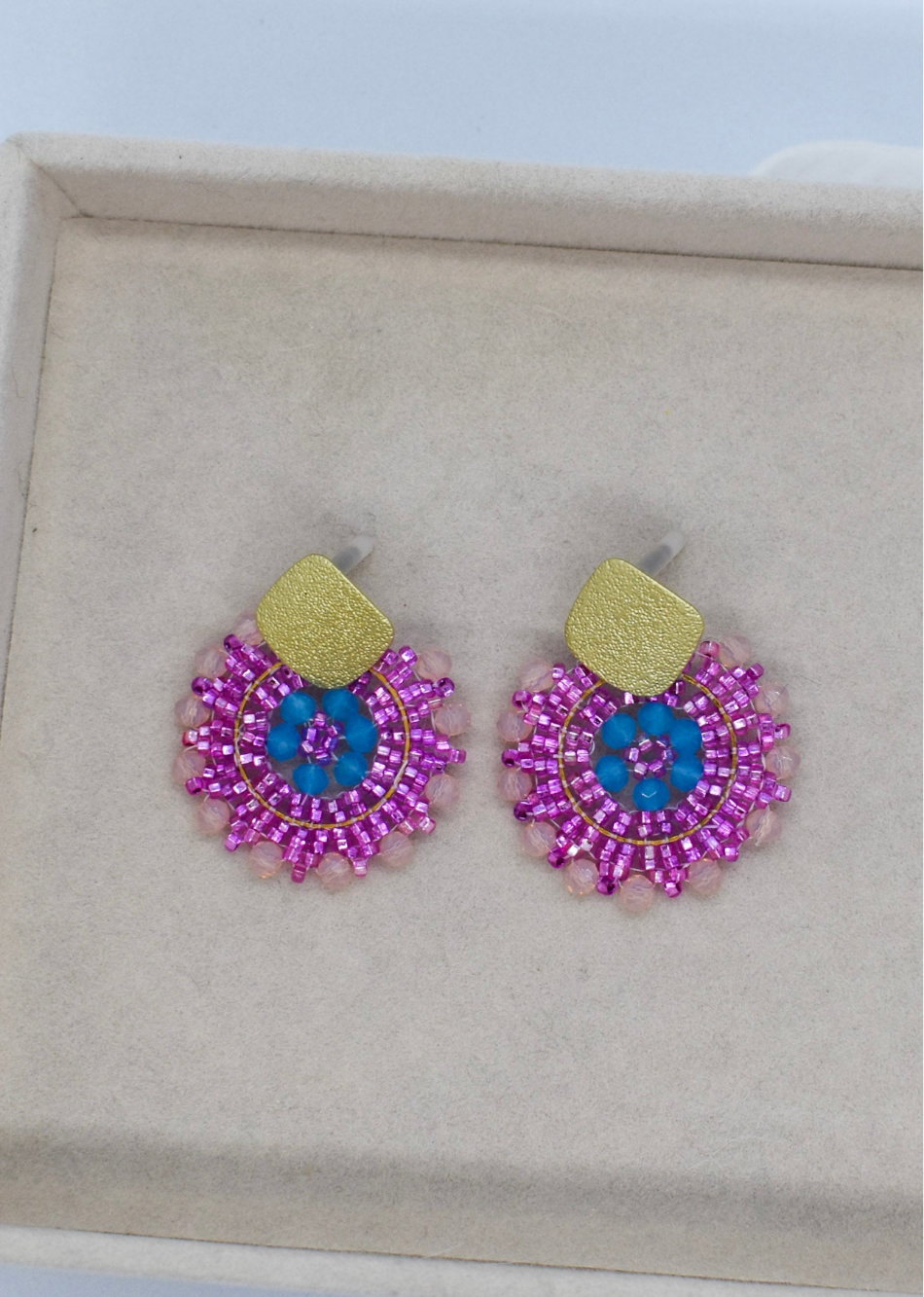 Pair of beaded earrings with pink and blue design on a beige display box.