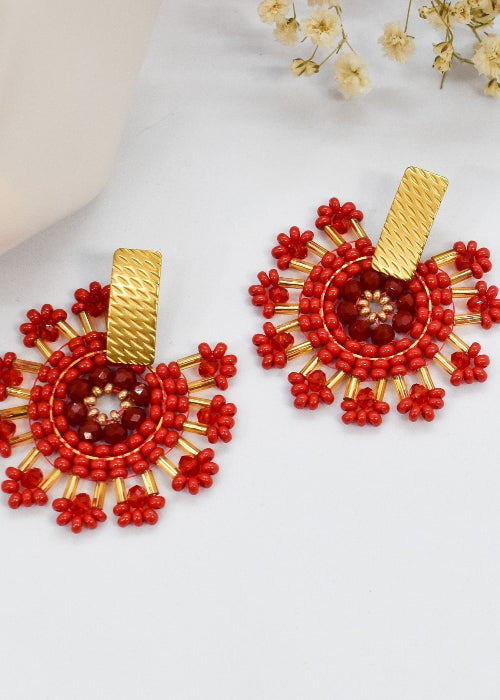 Red beaded earrings with gold accents on a white surface with dried flowers.