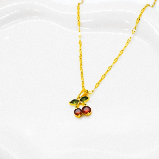 Gold necklace withred cherry pendant on a white dish