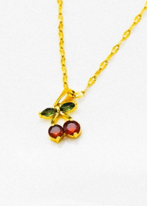 Gold necklace with green and red cerry strass charm on a white background
