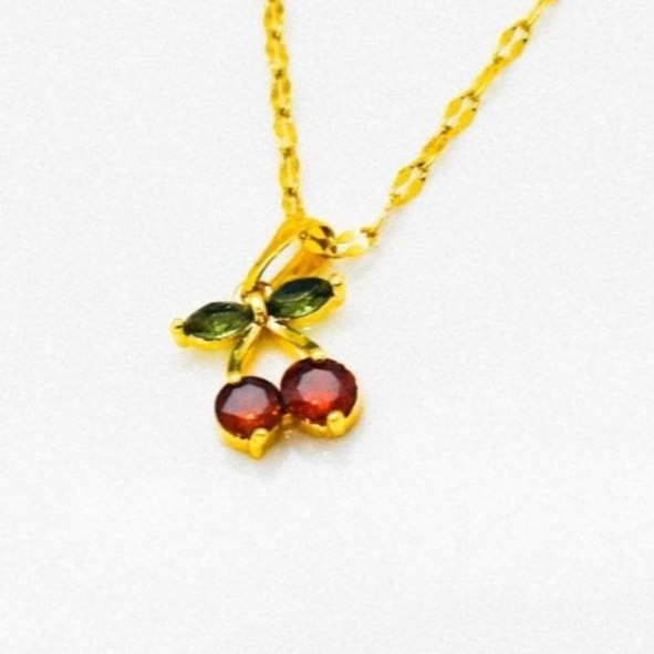 Gold necklace with green and red cerry strass charm on a white background