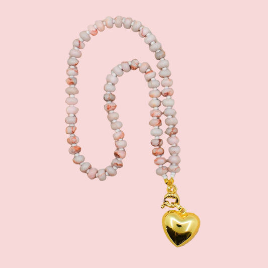 Necklace with pink beads and a gold heart pendant on a beige fabric background
