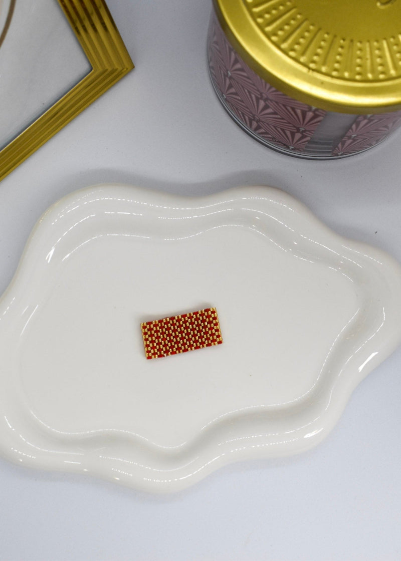 Small white dish with a rectangular pile of small brown beads on a white surface.