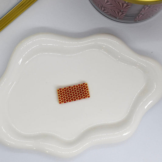 Small white dish with a rectangular pile of small brown beads on a white surface.