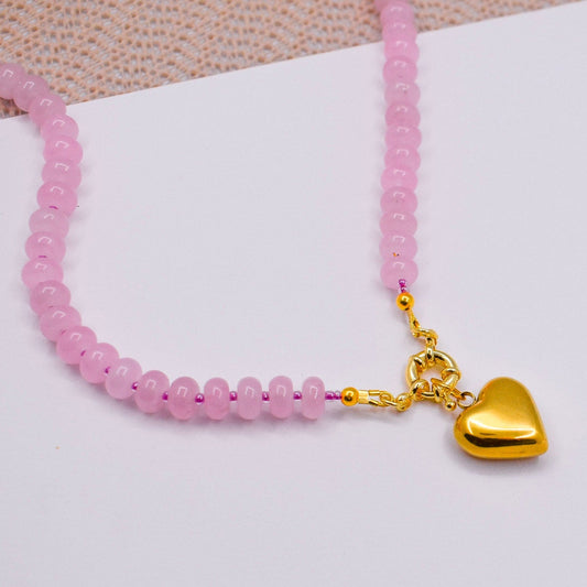 Rose quartz necklace with a gold heart charm on a white surface