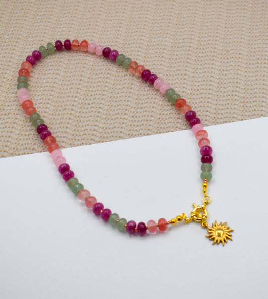Multicolored beaded bracelet with a gold sun charm on a beige fabric background