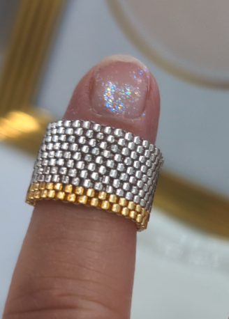 Finger wearing a gold and silver beaded ring on a neutral background