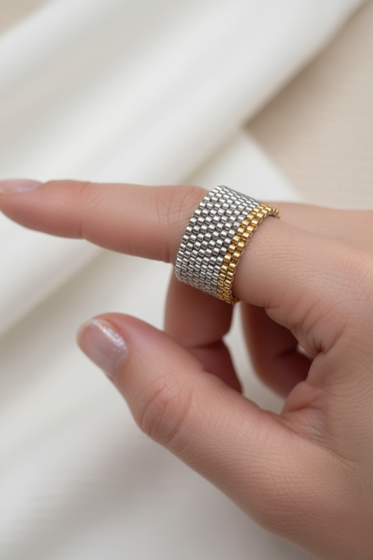 Finger wearing a gold and silver beaded ring on a neutral background