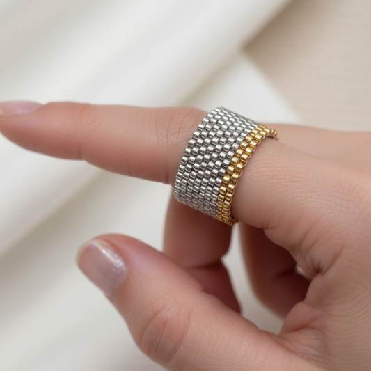 Finger wearing a gold and silver beaded ring on a neutral background