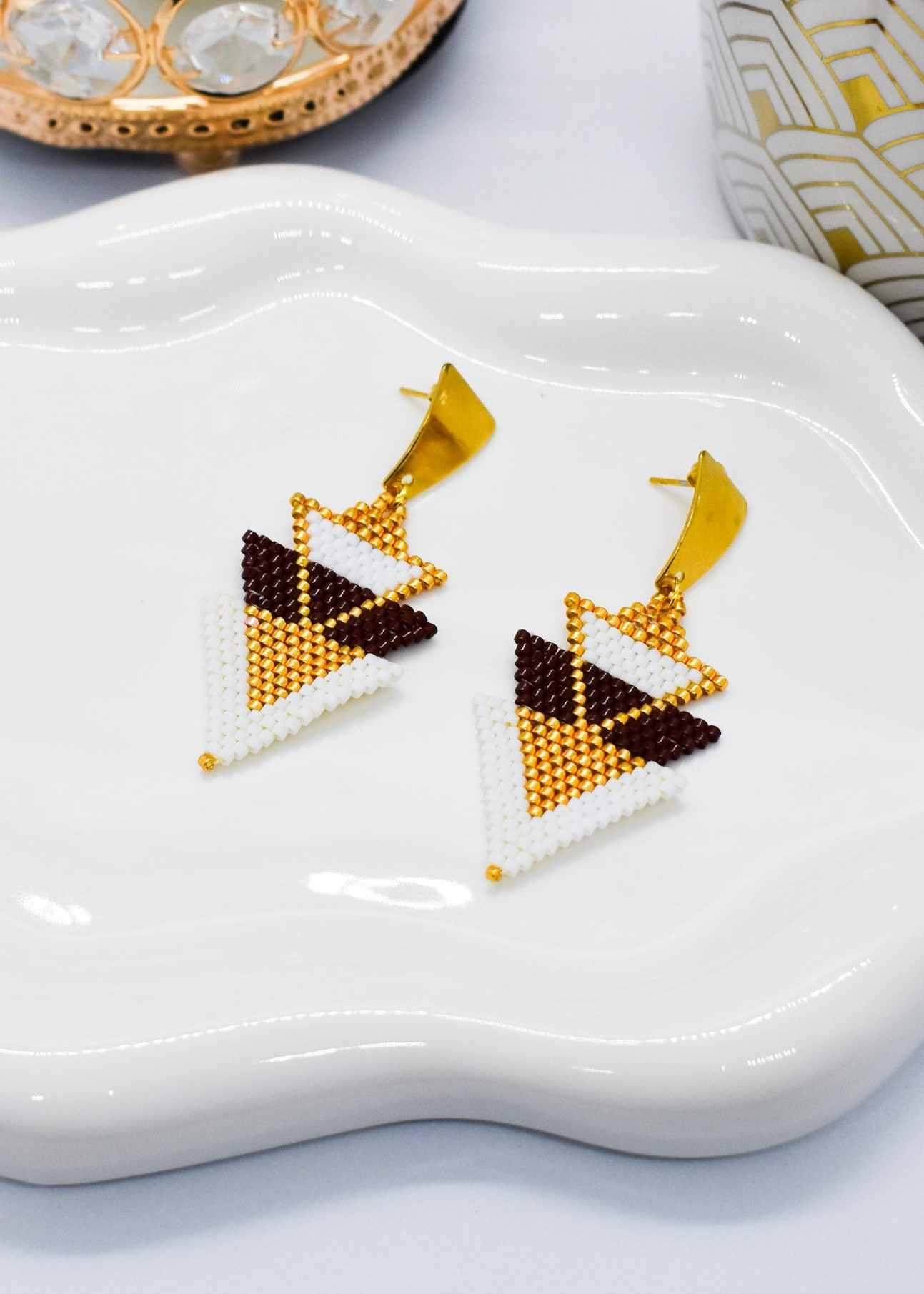 Triangular beaded earrings on a white dish with a decorative background