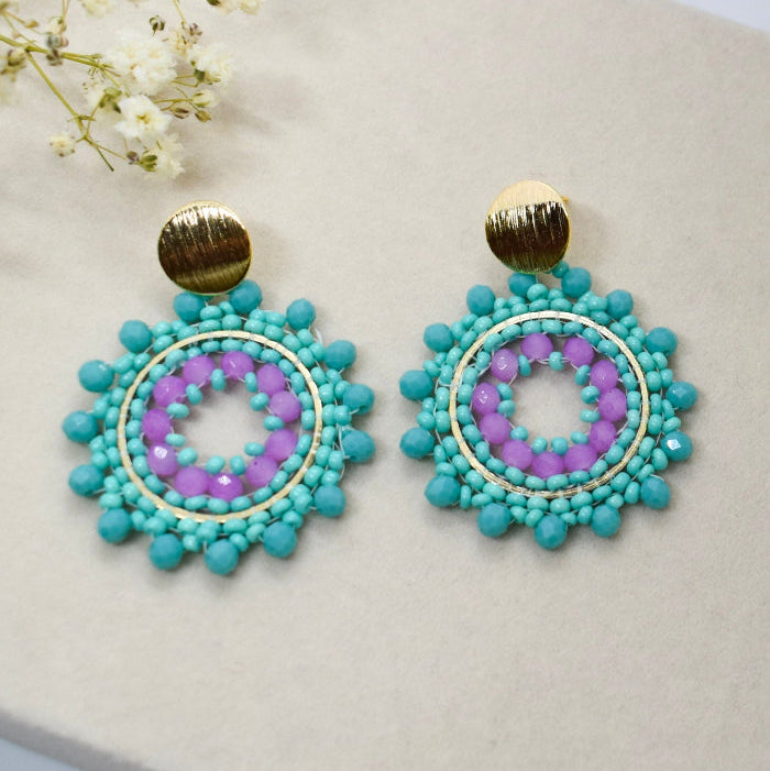 Turquoise and purple beaded earrings on a light surface with white flowers.