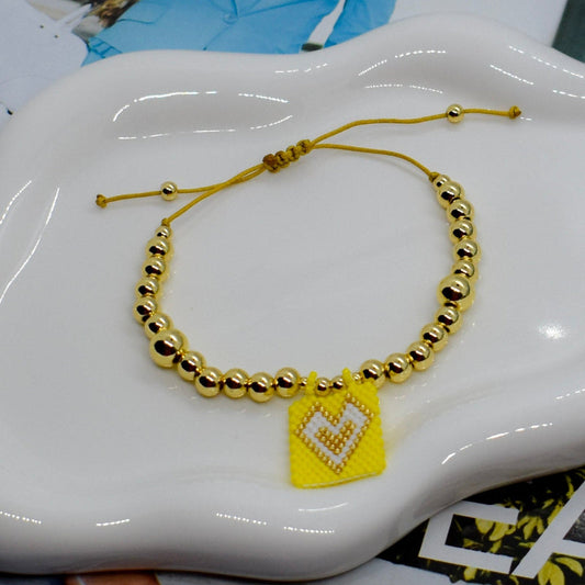Gold beaded bracelet with a yellow heart charm on a white dish.