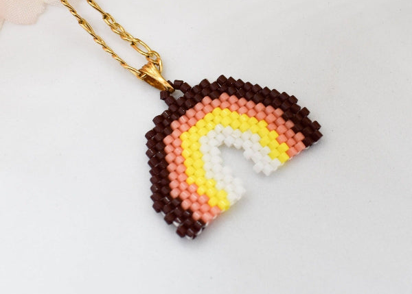 A colorful beaded bracelet with gold-tone charms, including a butterfly, evil eye, and heart, displayed on a white fabric jewelry pillow.