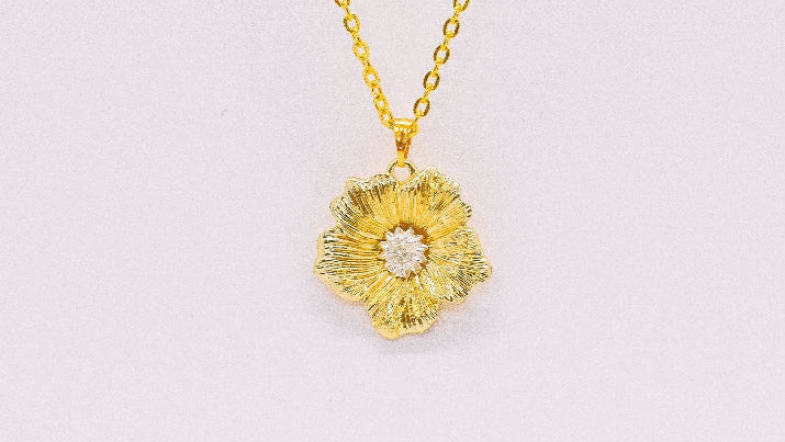Gold oval pendant necklace featuring a religious figure, surrounded by a border of small multicolored gemstones, displayed on a textured cream fabric background.