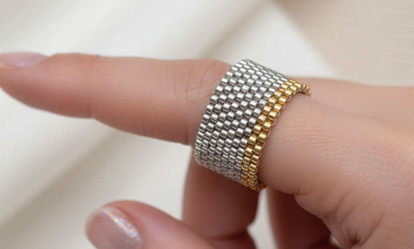 A close-up of a hand wearing a two-tone mesh ring with one silver-colored mesh band and one gold-colored mesh band.