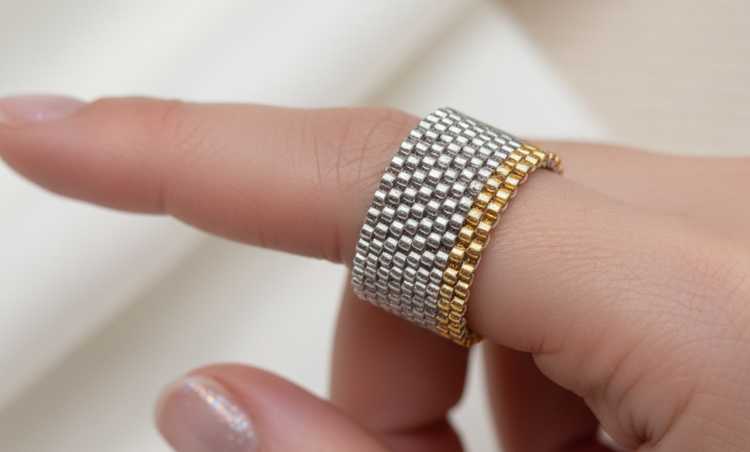 A close-up of a hand wearing a two-tone mesh ring with one silver-colored mesh band and one gold-colored mesh band.