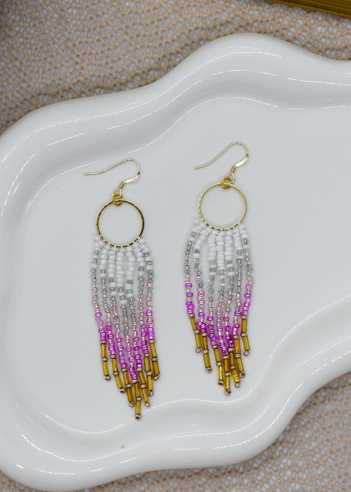 Beaded earrings with gold, pink, and purple on a white dish.
