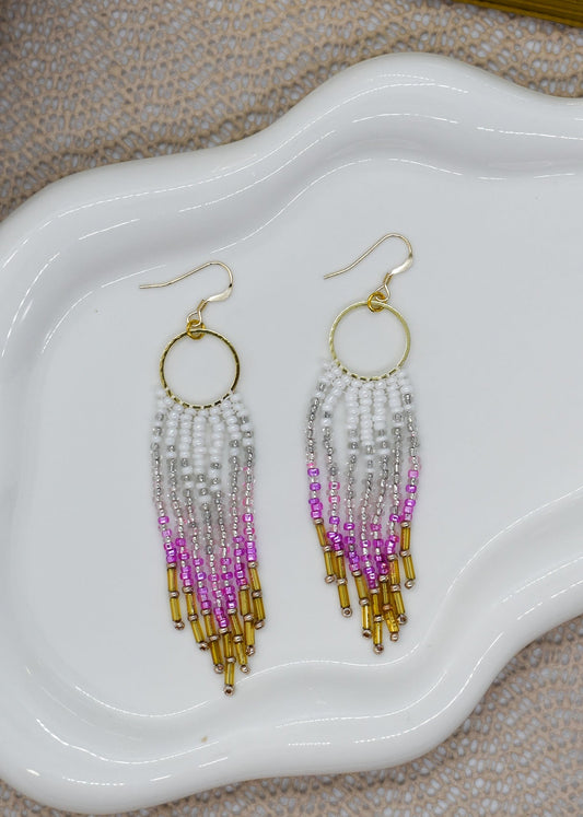 Beaded earrings with gold, pink, and purple on a white dish.