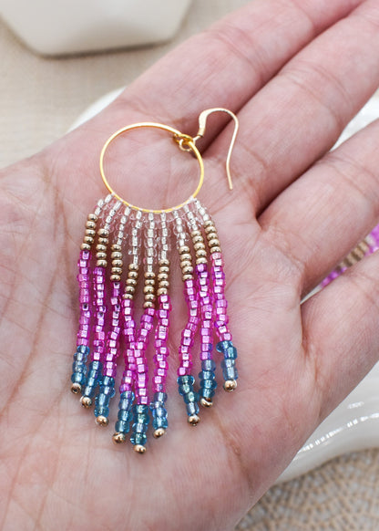 Beaded earrings with pink and blue gradient held in a hand.