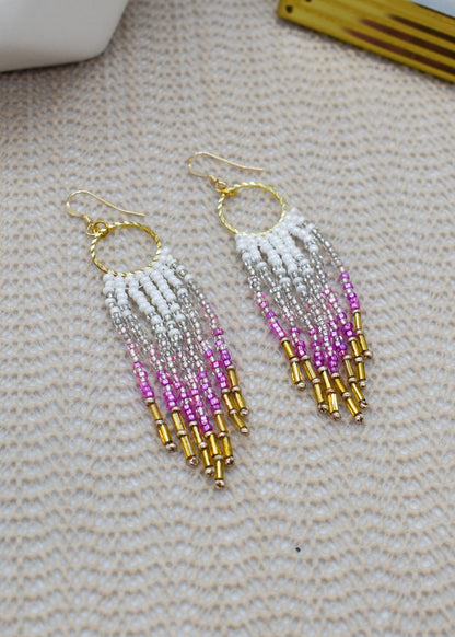 Beaded earrings with white, pink, and gold beads on a textured surface.