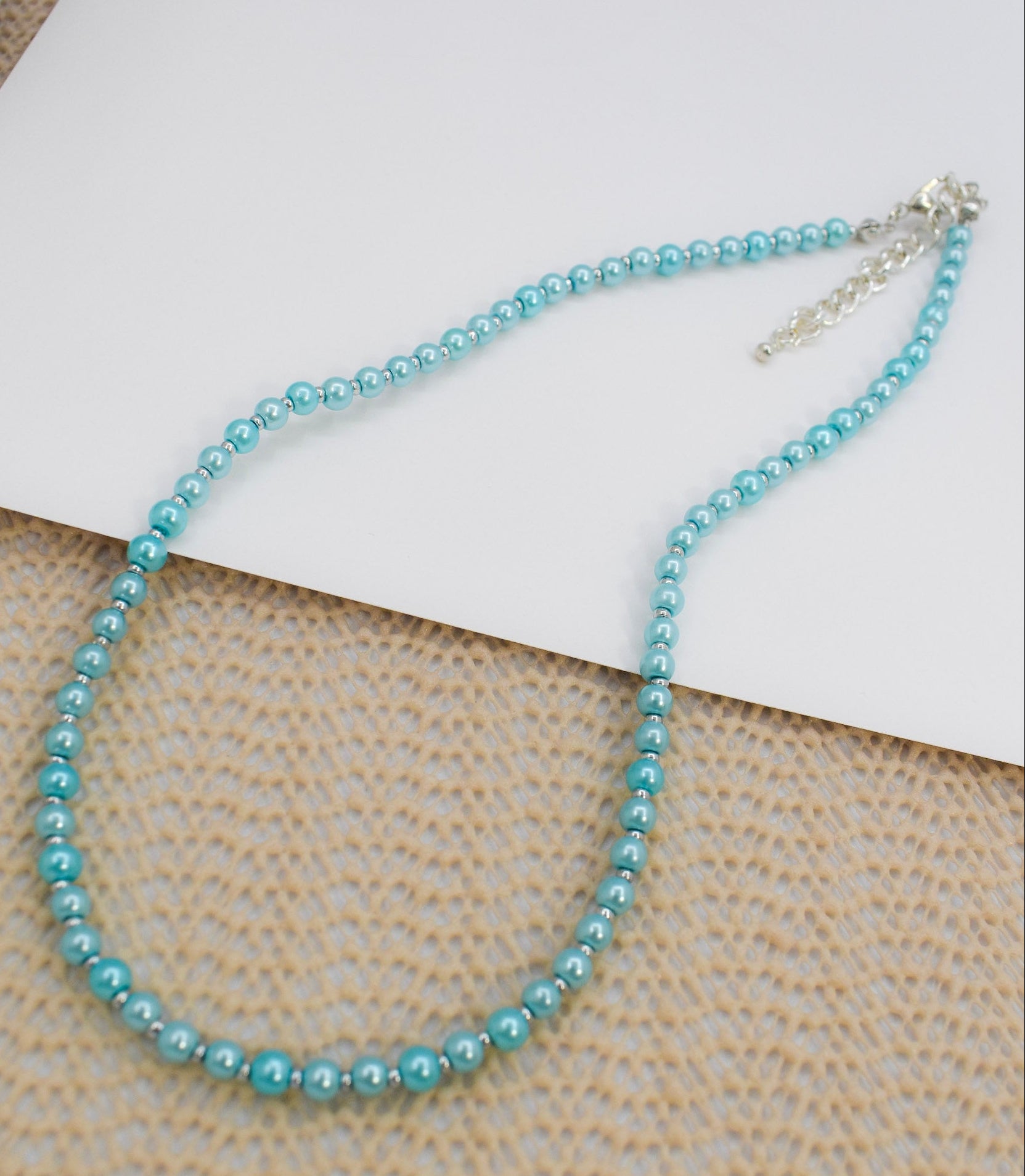 Blue beaded necklace on a textured surface with a white card