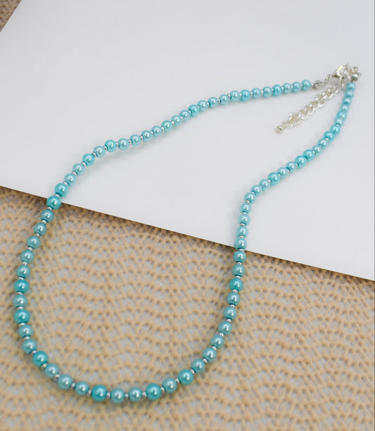 Blue beaded necklace on a textured surface with a white card