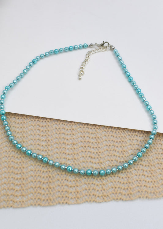 Turquoise pearl necklace on a textured surface with a white paper background