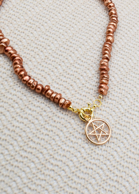 Brown beaded necklace with a pentacle charm  on a textured beige background