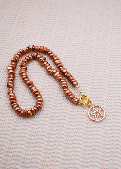 Brown beaded necklace with a gold pentagram pendant on a textured beige surface