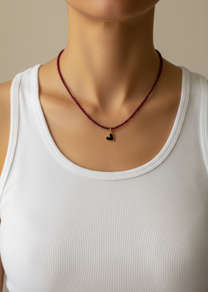 Person wearing a red beaded necklace with a heart pendant on a beige background