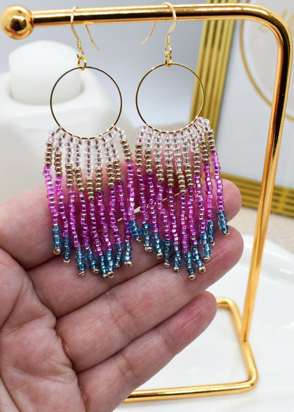 Colorful beaded earrings held in a hand with a gold stand in the background