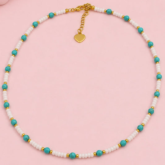 Necklace with white beads and turquoise accents on a pink surface