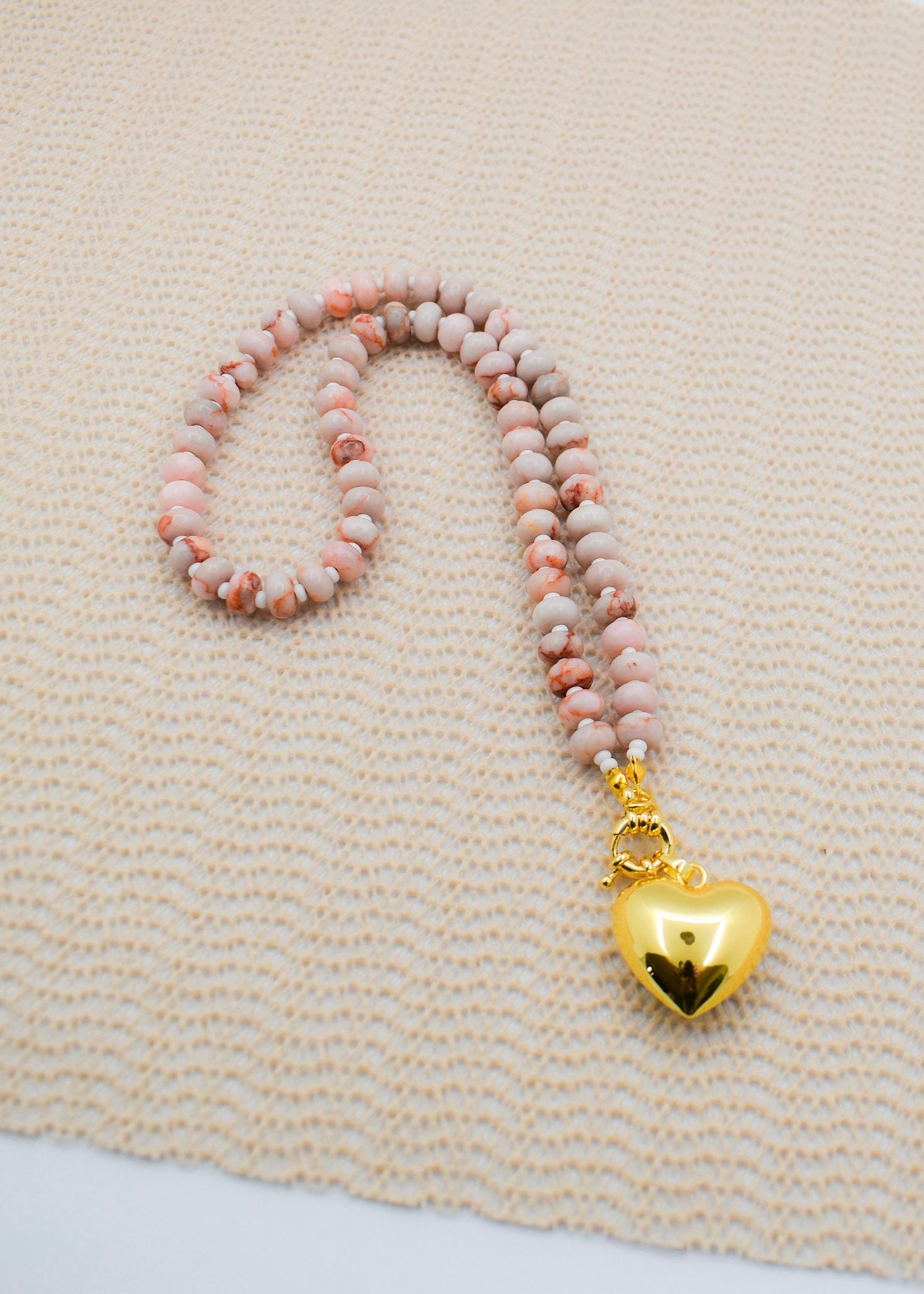 Beaded necklace with a gold heart pendant on a textured beige surface
