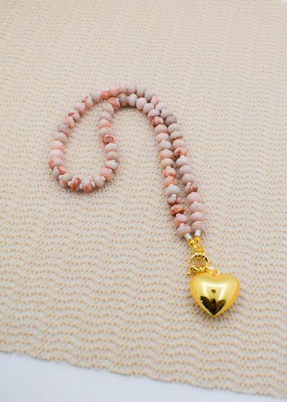 Beaded necklace with a gold heart pendant on a textured beige surface