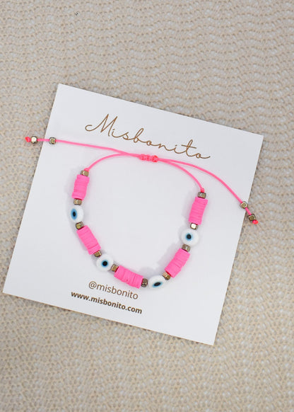 A pink beaded bracelet with evil eye beads displayed on a white card labeled Misbonita, set against a textured beige background.