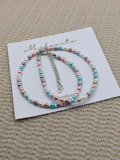 A beaded bracelet with pastel pink, blue, purple, and white pearls on a silver chain, displayed on a white card printed with the brand name 'Misbonita' on a textured beige woven background.