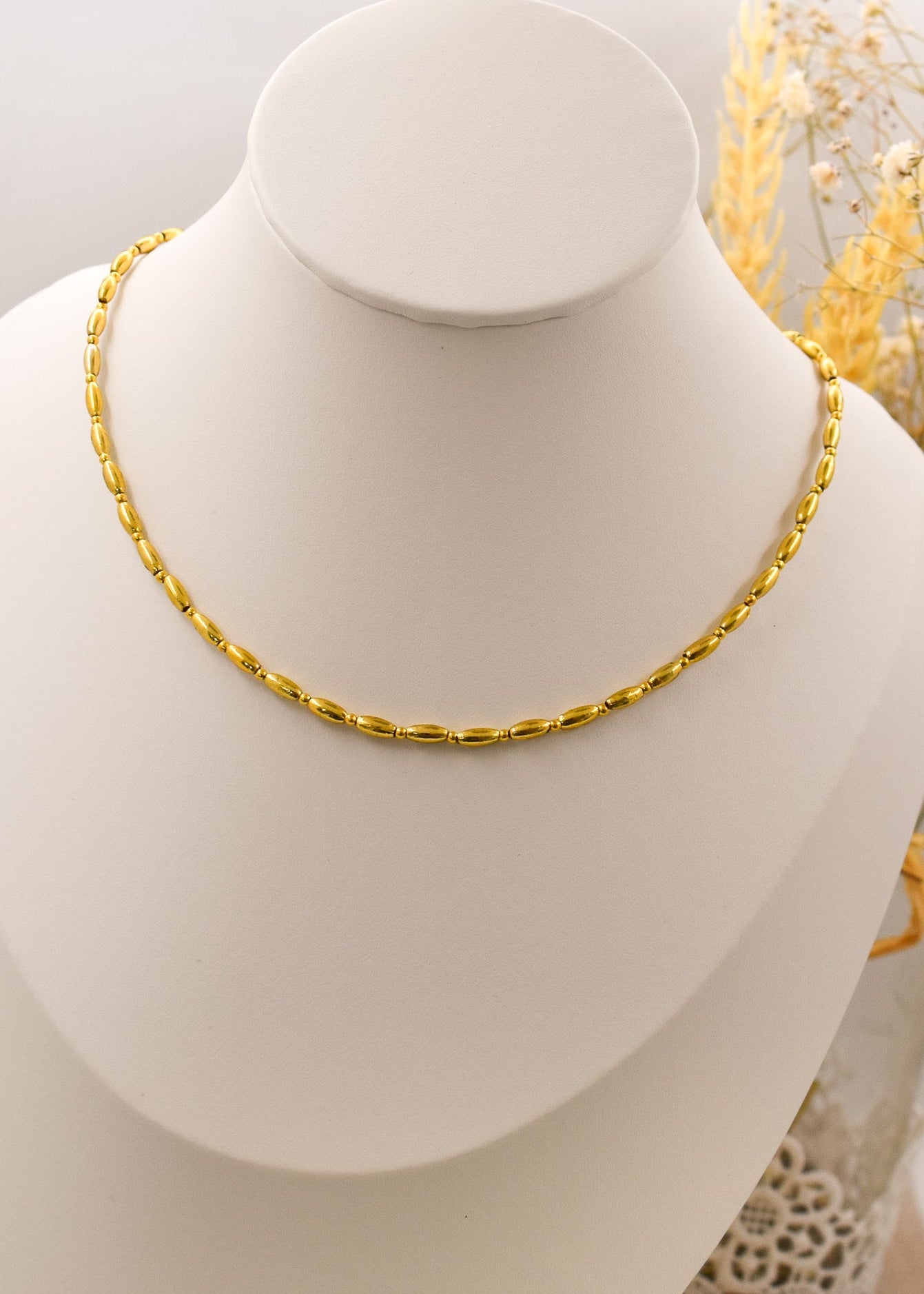 Gold necklace on a white mannequin bust with a neutral background