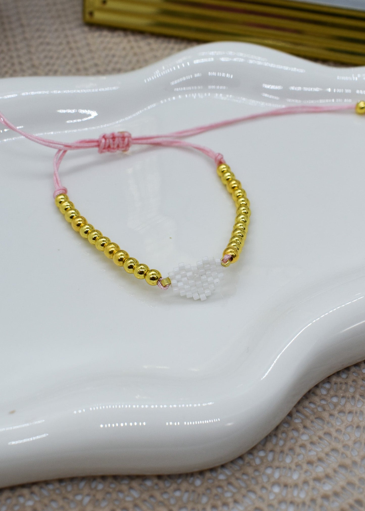 Gold beaded bracelet with pink string on a white dish